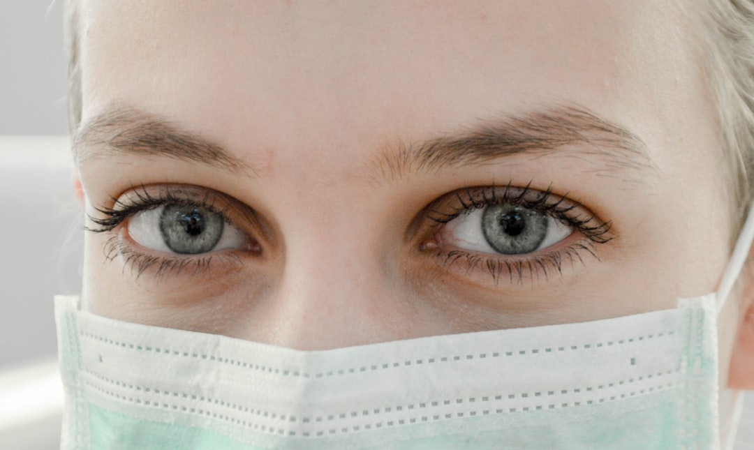 Close-up of a person's face wearing a light green medical mask, showing brighter eyes and light skin.