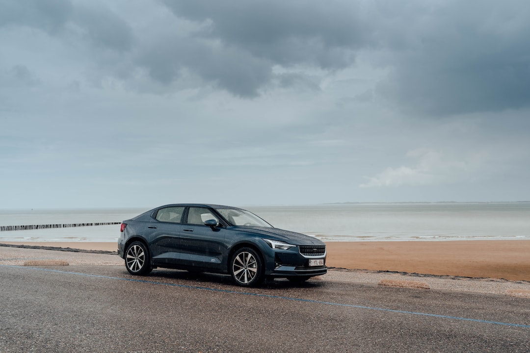 A dark blue sedan, symbolizing the future of luxury travel, is parked on a wet road by a beach under a cloudy sky.
