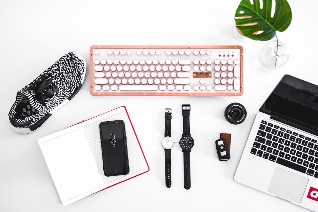 A workspace with a pink keyboard, black-and-white sneaker, open notebook, smartphone, mechanical watches, camera lens, car key, and laptop on a white surface with a green plant leaf—blending digital age vibes with a touch of renaissance style.