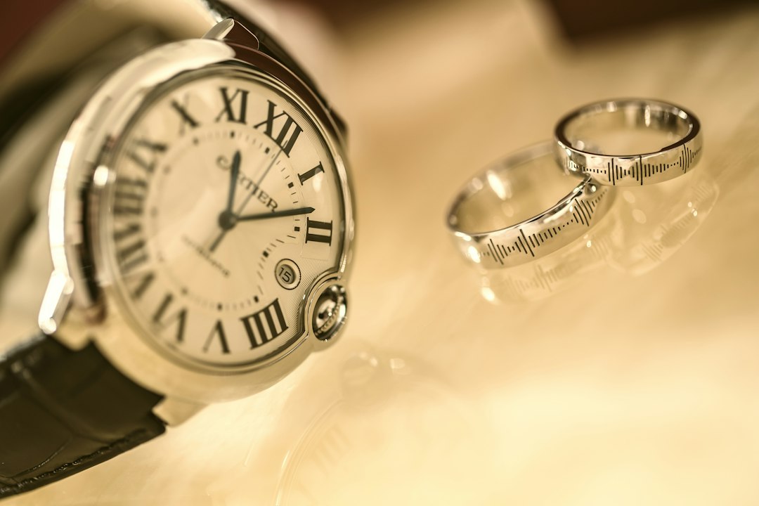 A close-up of a Cartier wristwatch with Roman numerals next to two silver rings on a beige surface, perfect to elevate your look and accessorize with timeless fashion jewelry.