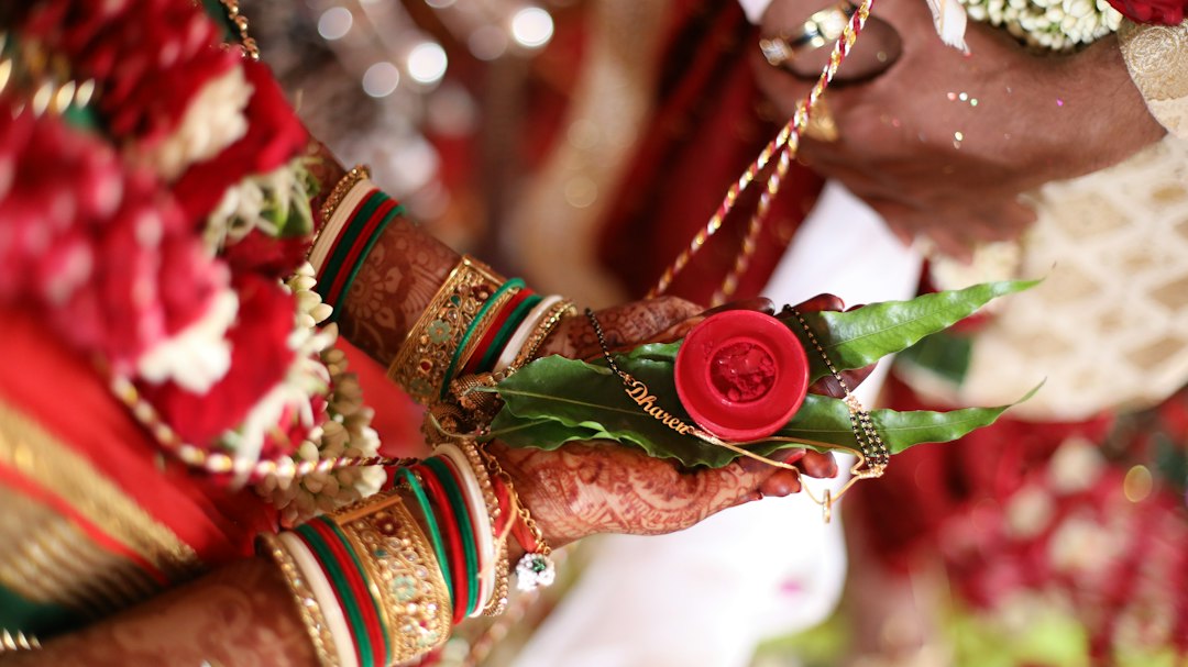 Close-up of a bride’s hands with henna, bangles, wedding accessories, and jewelry holding green leaves and a red item during a traditional Indian wedding ceremony.