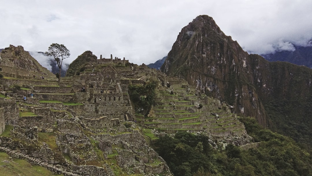 Explore ancient stone ruins of Machu Picchu with terraced slopes and a towering peak, all under a cloudy sky—an experience rivaling the Aztec Luxury found on Exclusive Tours from Mexico City.