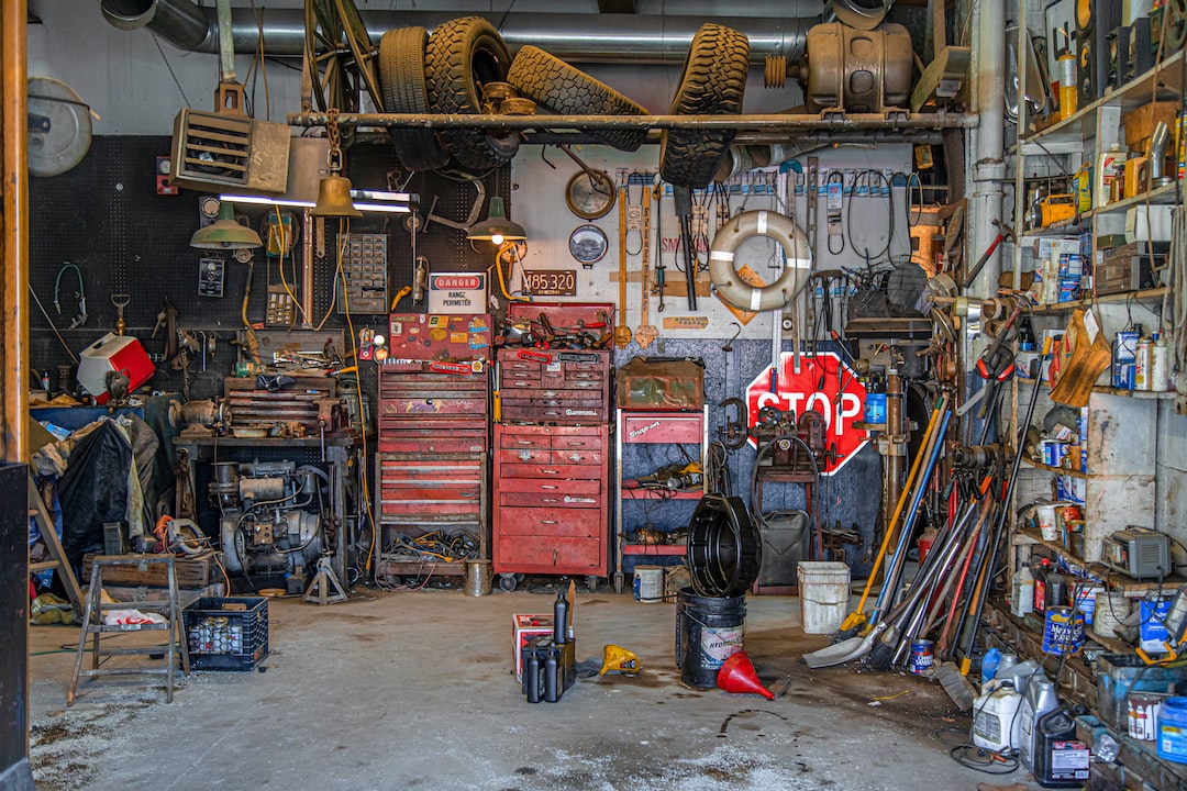 Cluttered workshop with red tool chests, various tools, tires hanging overhead, shelves stocked with supplies, and a stop sign leaning against the back wall—perfect for custom car design and creative car customization projects.