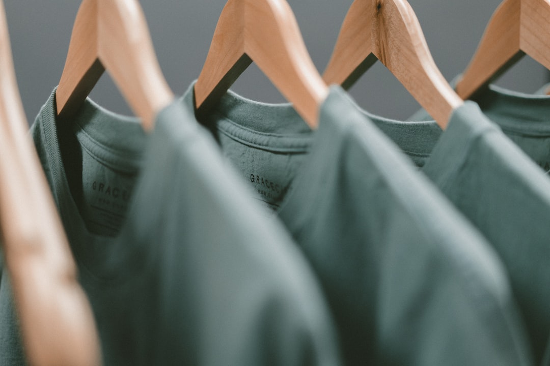 Four green t-shirts are neatly hung on wooden hangers, arranged in a row, offering a behind the scenes glimpse into haute couture with a softly blurred background.