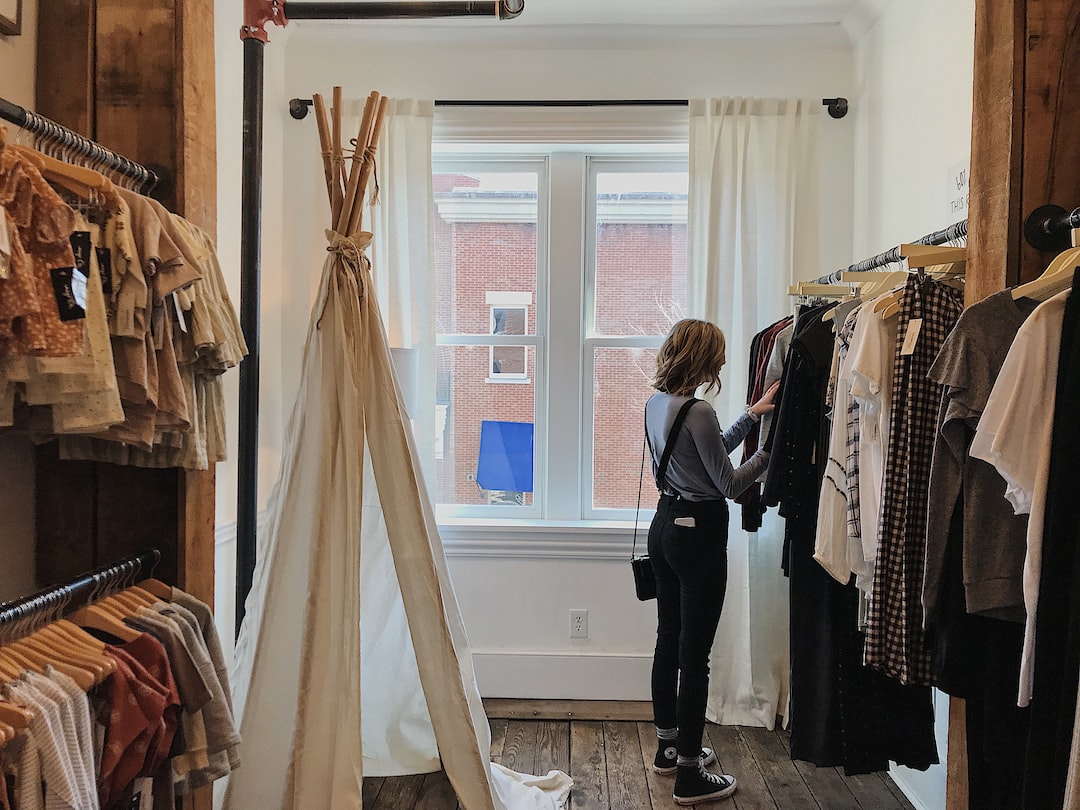 A person stands by a clothing rack in a small boutique, viewing garments near a large window with white curtains and a brick building outside—capturing the chic ambiance of exclusive designer stores in Berlin high fashion.