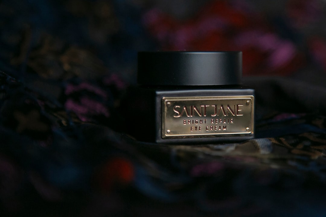 A jar of Saint Jane Bright Repair Eye Cream with a gold label, enriched with Vitamin C, set against a dark, blurred background.