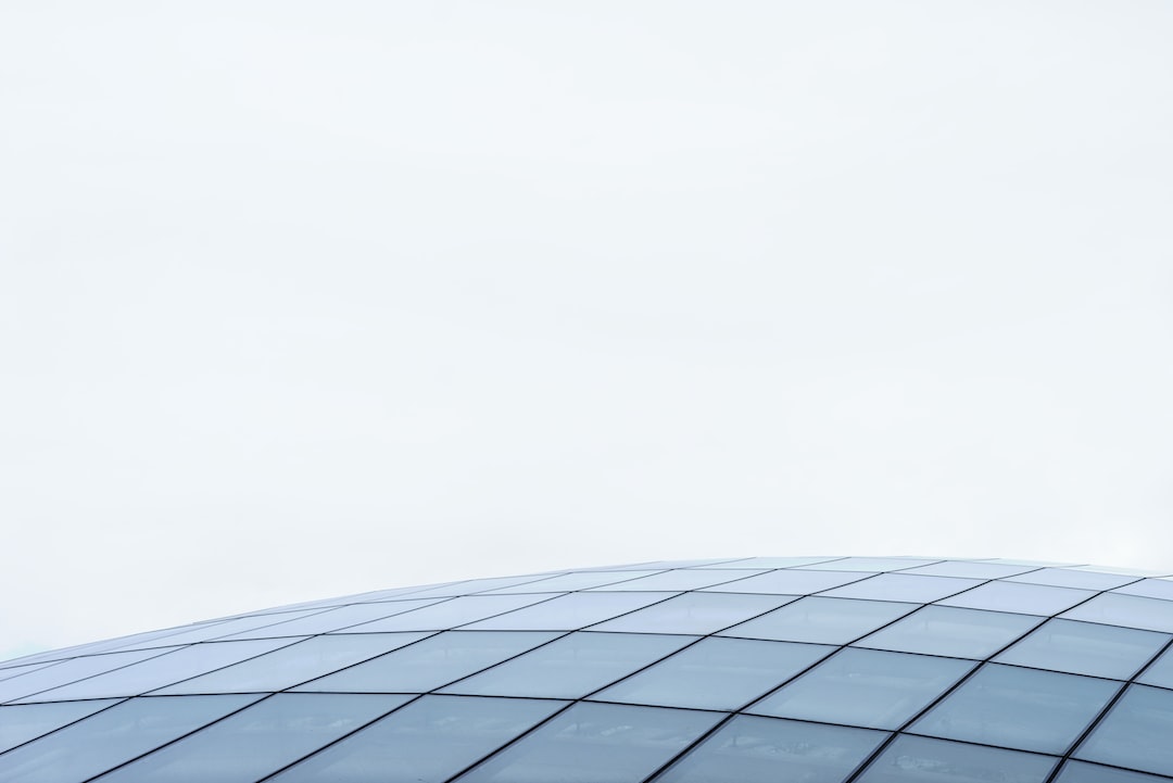 Curved glass building with a grid pattern against a pale, overcast sky, showcasing modern flair.