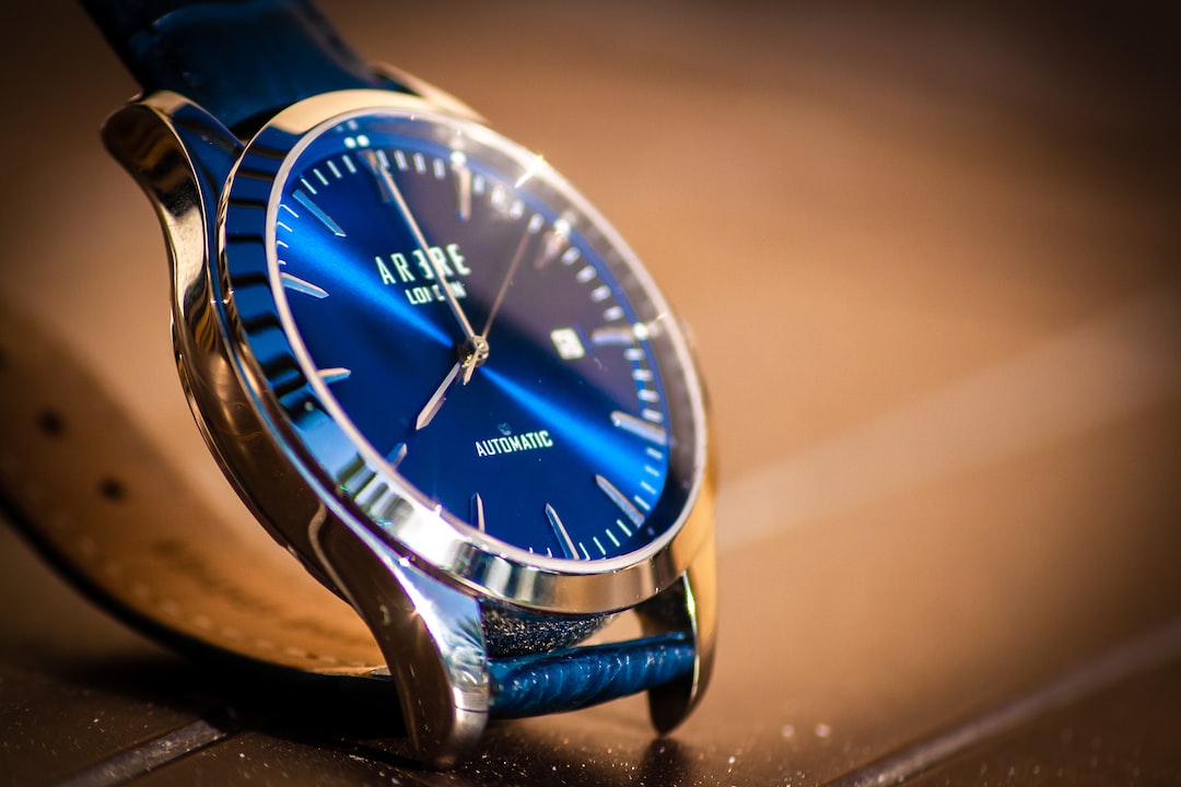 Close-up of a Cartier blue-faced wristwatch with silver casing and leather strap, displaying the time and date on a wooden surface—a refined addition to luxury timepieces.