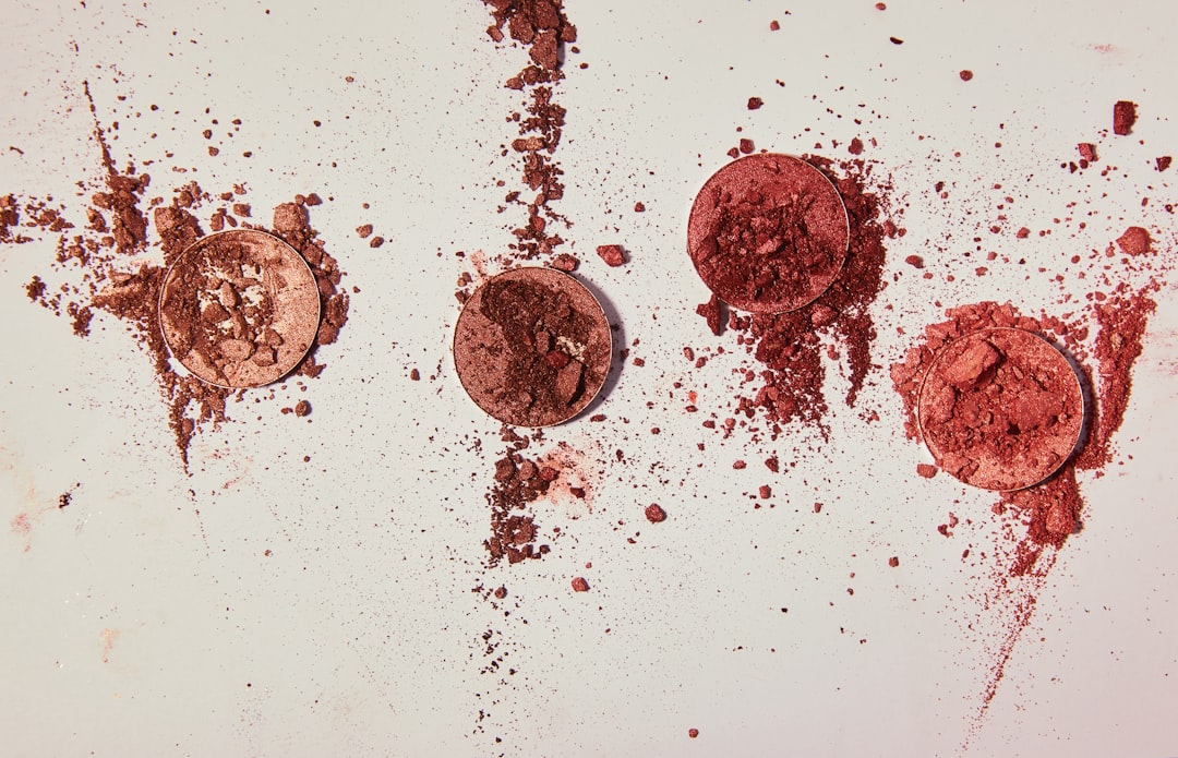 Four broken makeup powder compacts in shades of brown and red are scattered on a light surface, their fragments spread around—perfect for a Beauty Box Comparison or exploring new shades through beauty box subscriptions.