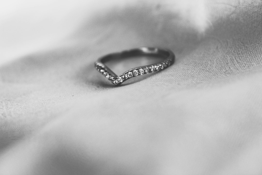 A silver ring with a V-shaped band and small diamonds, embodying timeless elegance, rests on a soft, light-colored fabric surface.