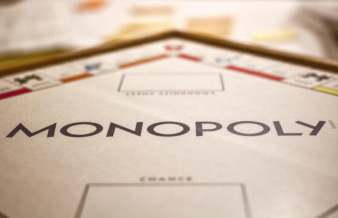 Close-up of a Monopoly game board showing the logo and part of the playing area, with blurred game pieces and cards in the background—echoing how giants like De Beers have shaped the global diamond industry’s landscape.
