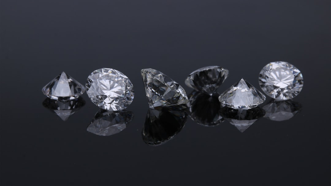 Six round-cut diamonds from De Beers are arranged on a reflective black surface, showcasing their brilliant facets and epitomizing luxury jewelry.