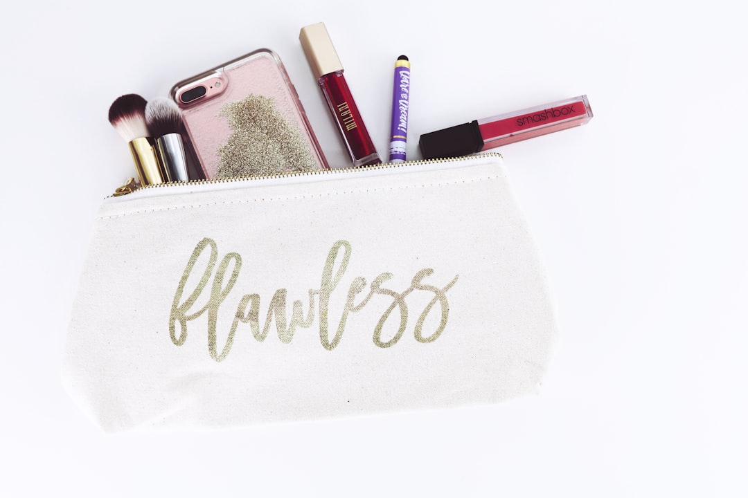 A makeup bag labeled "flawless" is unzipped, revealing brushes, lipstick, lip gloss, a phone, and other cosmetics spilling out—your toolkit for debunking Beauty Myths with every look.