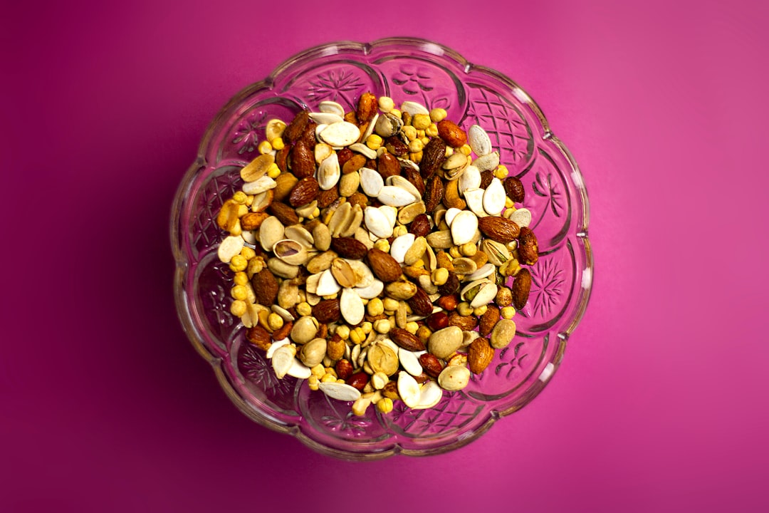 A glass bowl filled with a mix of assorted nuts and seeds—perfect natural beauty boosters—sits on a solid pink background.