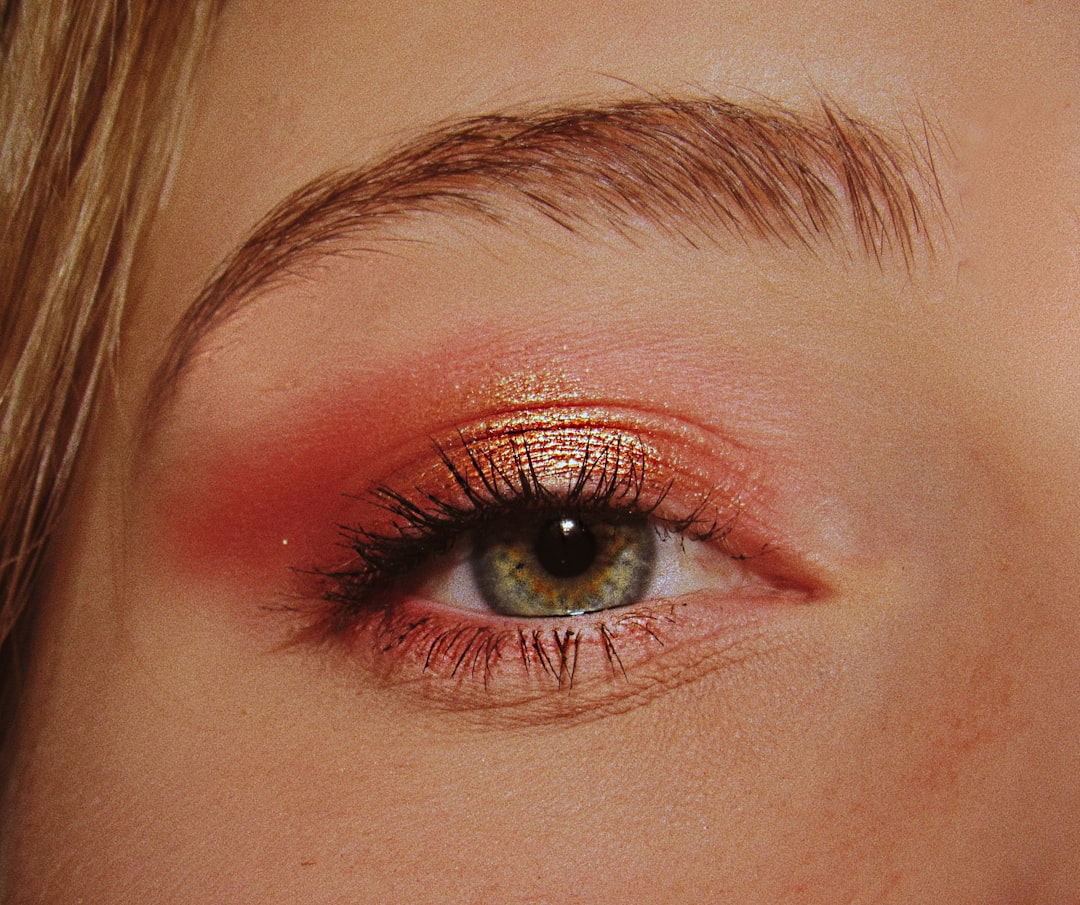 Close-up of a green eye with long lashes and shimmery orange eyeshadow, highlighting detailed eyebrow and skin texture—perfect inspiration for your everyday makeup or Alltags-Make-up routines.