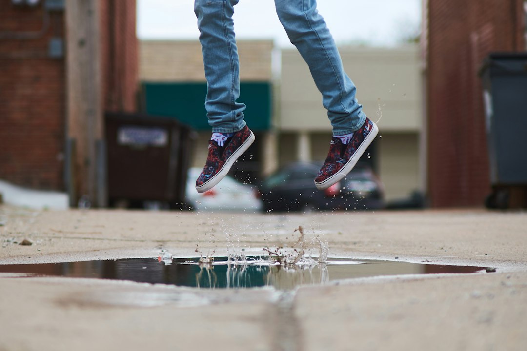 A person jumps above a puddle on a concrete alleyway, water splashing up where their feet left the surface—captured during one of our high-end photography expeditions.