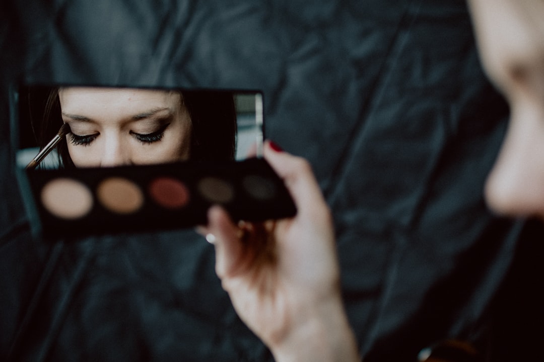 A person holds a must-have Pinsel eyeshadow palette and applies makeup, reflected in a small rectangular mirror with eyes closed, aiming for a flawless look.