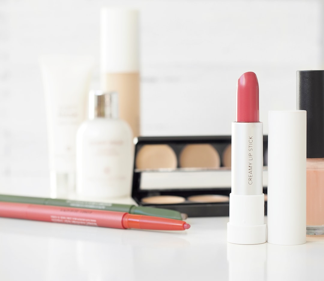 A collection of cosmetics for effortless beauty, including pink lipstick, eyeliner pencils, eyeshadow palette, nail polish, foundation, and lotion, all arranged on a white surface—perfect for your everyday makeup routine.