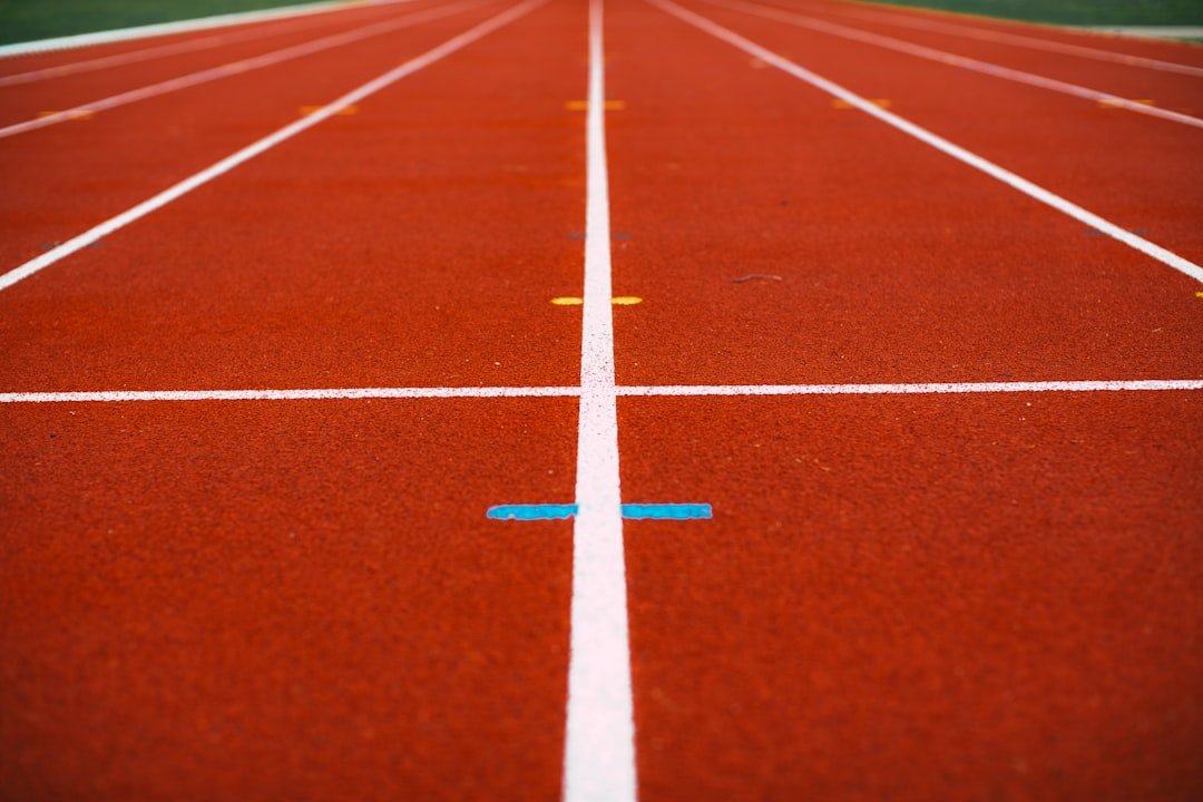 Close-up view of red running track lanes with white dividing lines, colored markers, and a green field in the background—an exclusive setting near luxury living and city villas for rent.