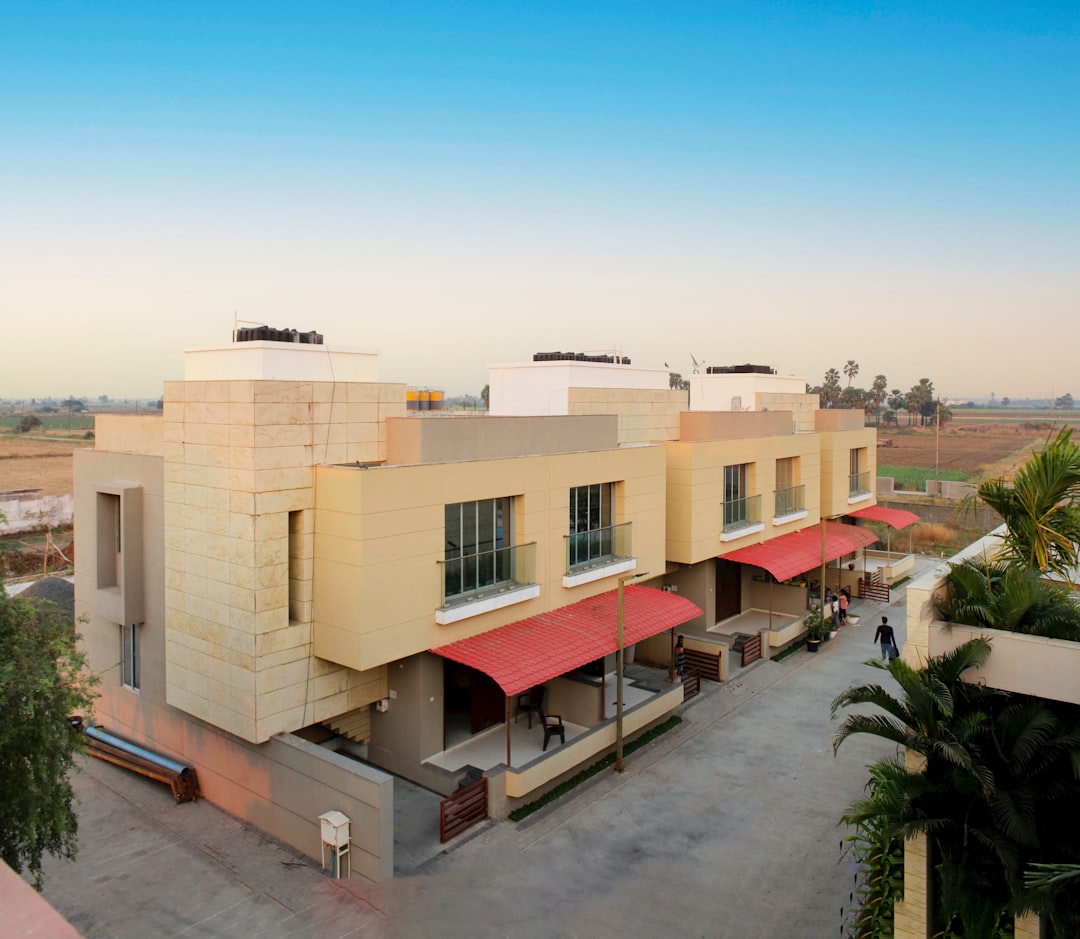 Two modern, beige townhouses with red awnings and rooftop structures sit on a paved driveway against a rural landscape and clear blue sky—a quiet paradise that feels worlds away from the famed overwater bungalows of exotic Hochzeitsreisen destinations.