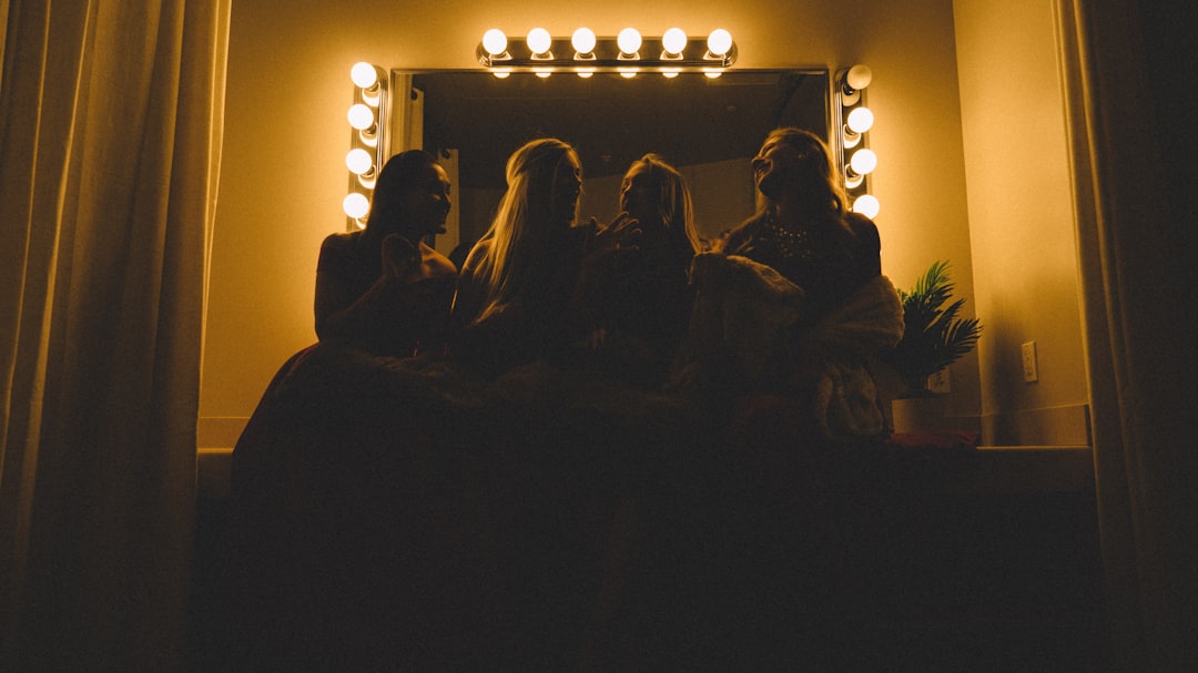Four women sit together in front of a large, illuminated vanity mirror at an exklusive Casino-Resort, their faces dimly lit and mysterious—capturing the essence of luxury for the elite traveler.