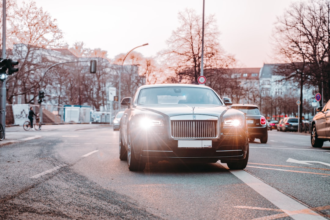 A black Rolls-Royce with headlights on glides down a city street among other cars during the day, exuding the elegance of Underwater Luxury found in top Tauchresorts.