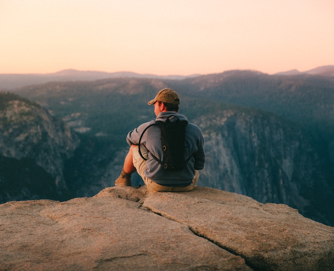 A person wearing a backpack sits on a rocky ledge overlooking a scenic mountain landscape at sunset, capturing the breathtaking beauty found in national parks.