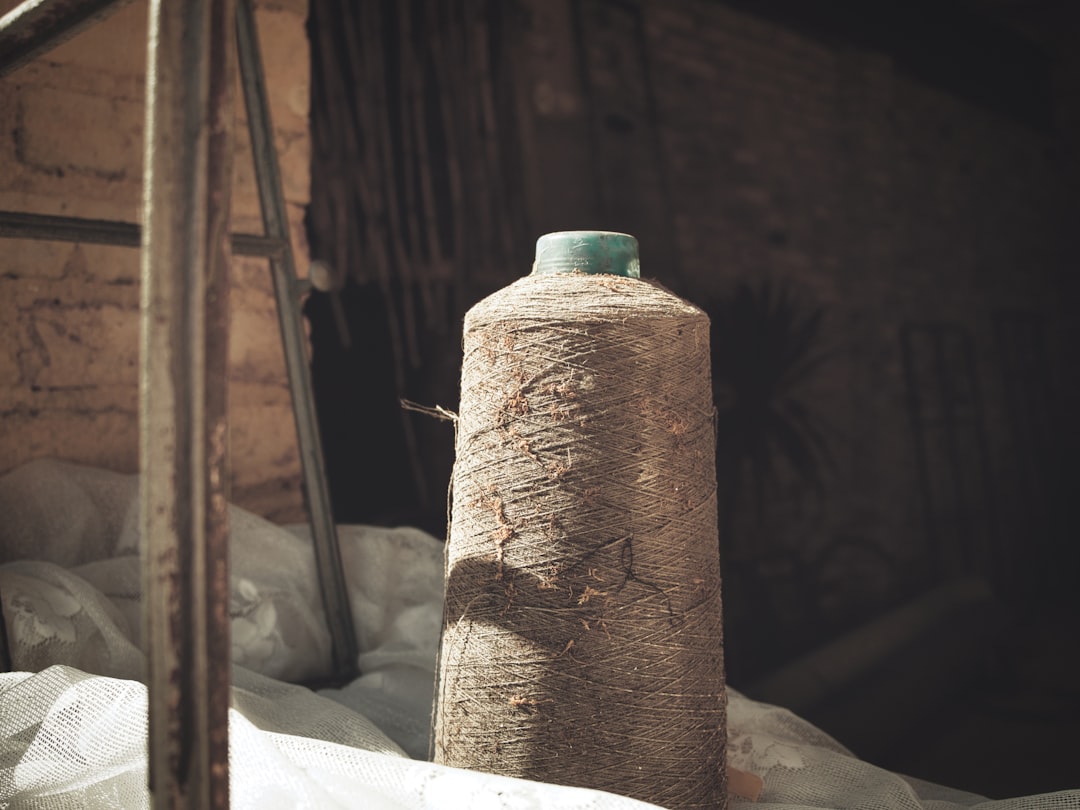 A large spool of rough, brown twine sits on white fabric in a dimly lit industrial setting, evoking the tactile detail often explored during high-quality art and literature tours.