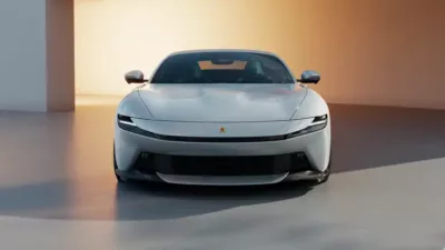 Front view of a luxury silver sports car parked on a smooth, light-colored surface with a gradient beige and white background.