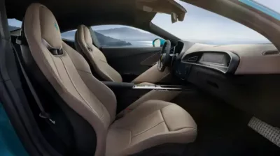 Interior view of a luxury modern sports car with beige leather seats, digital dashboard, and a scenic coastal landscape visible through the windows.