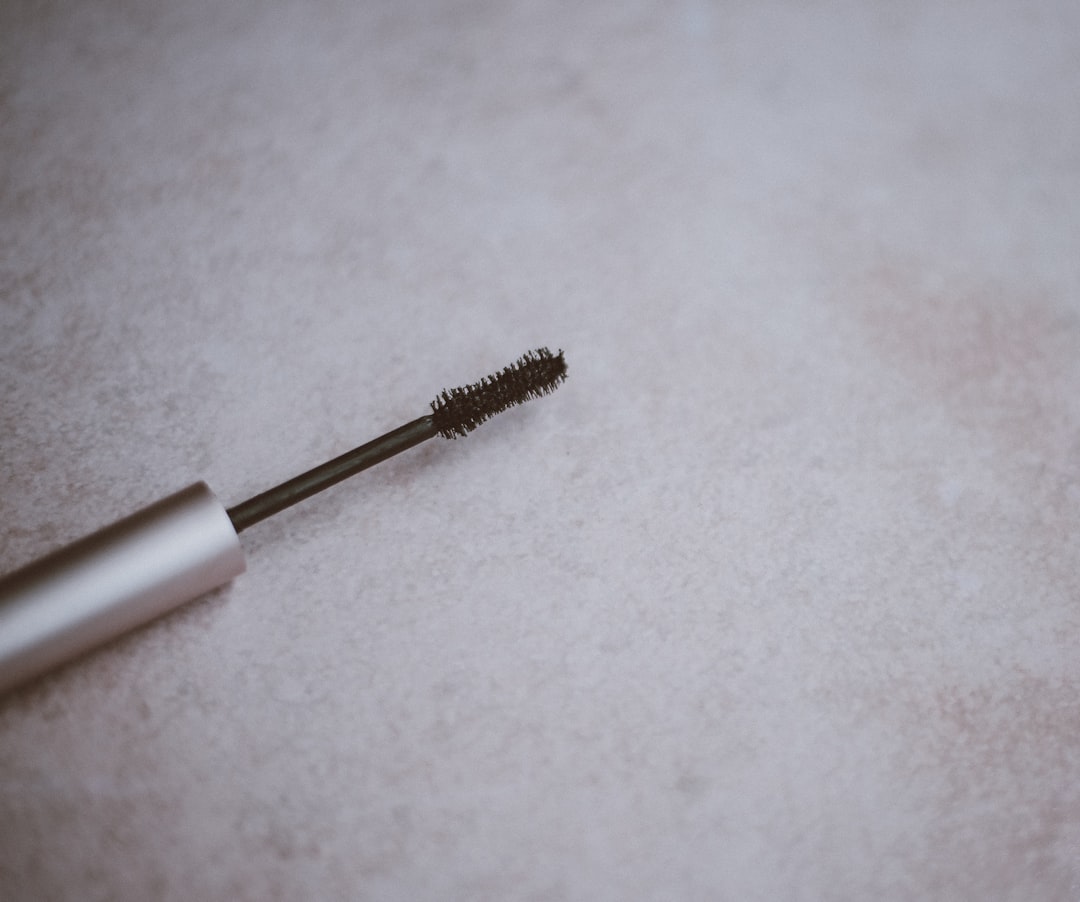 A close-up of a mascara wand with a silver handle, lying on a light, textured surface—perfect for flawless mascara application and ensuring no more clumps.
