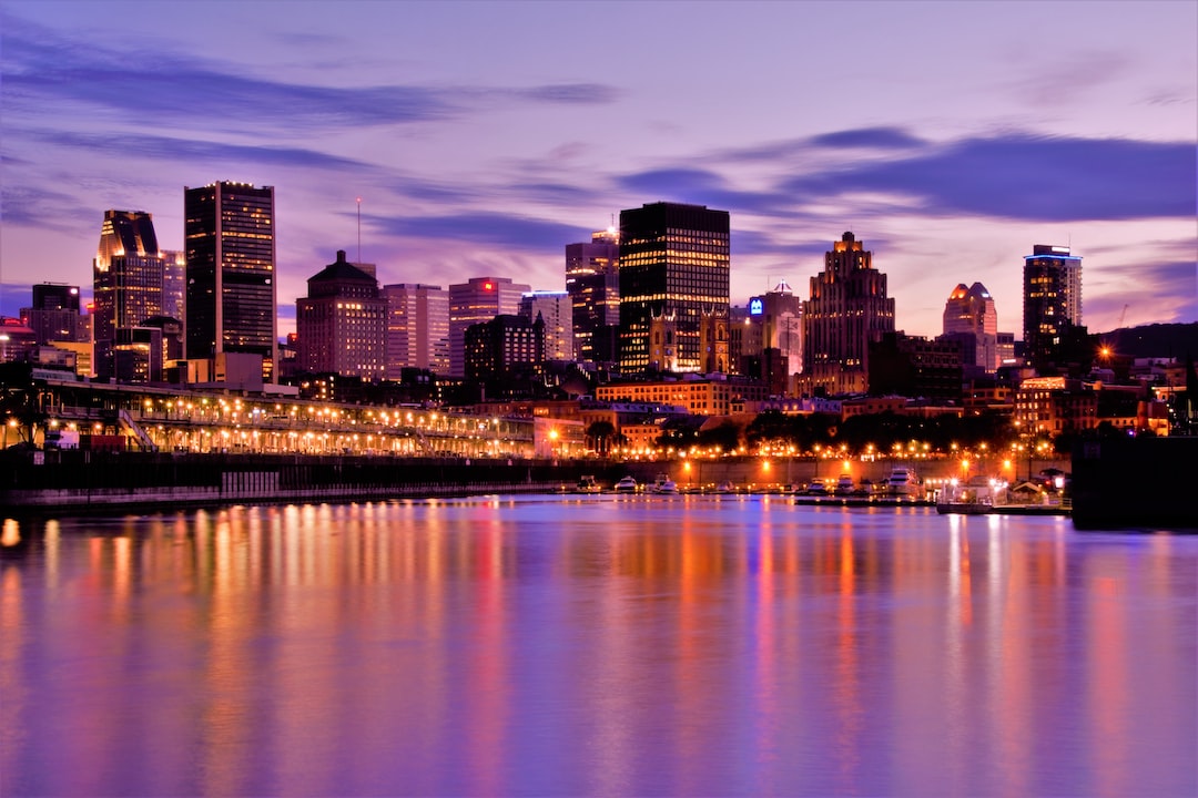 City skyline at dusk with illuminated buildings reflected in a calm body of water, under a purple and blue sky, capturing the luxury experiences and French-Canadian charm of Old Montreal.
