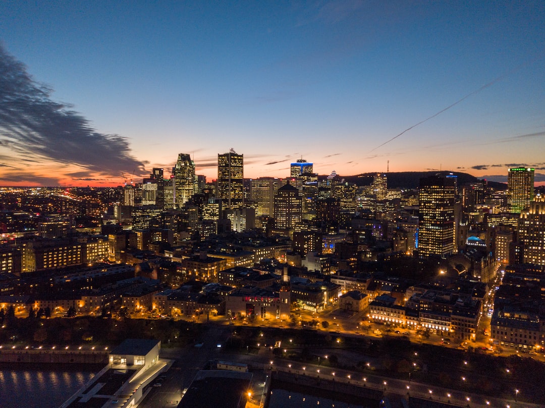 Aerial view of a city skyline at dusk with illuminated buildings and a partly cloudy sky, capturing the French Canadian Elegance and charm of Old Montreal.