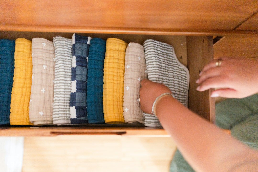 A person arranges neatly folded, colorful cloths in a wooden drawer, creating the perfect space for organized jewelry or stylish jewelry storage.