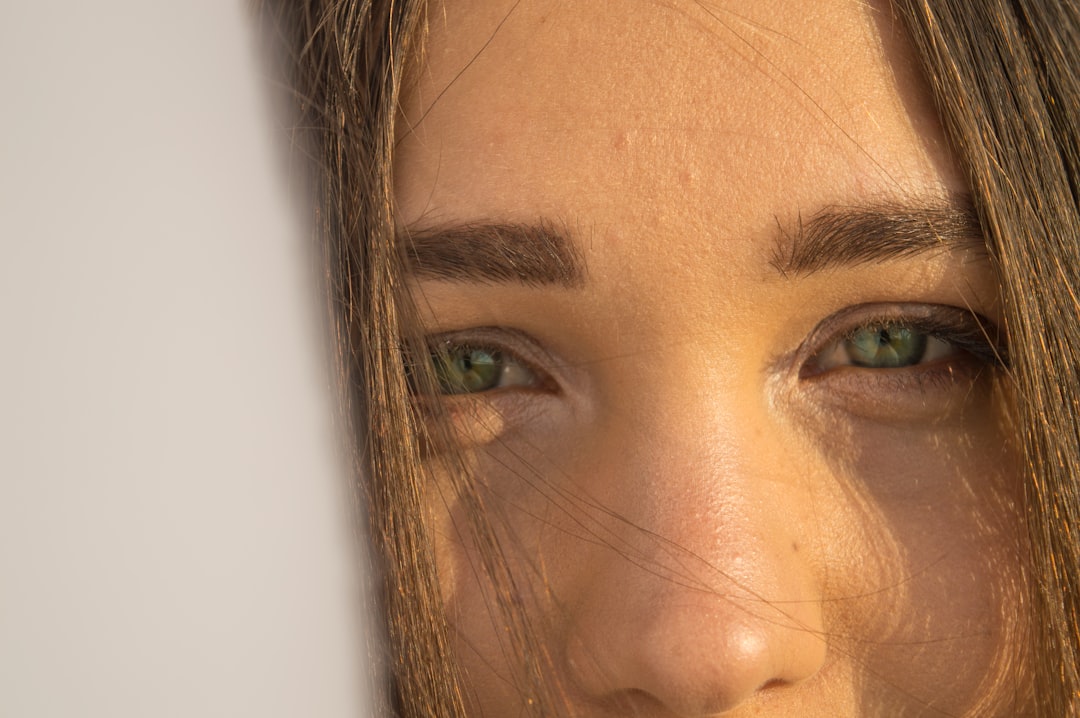 Close-up of a person's face focusing on their green eyes and eyebrows, with part of their face partially obscured by a white surface—perfectly capturing the allure of Haarfarben-Trends 2024.