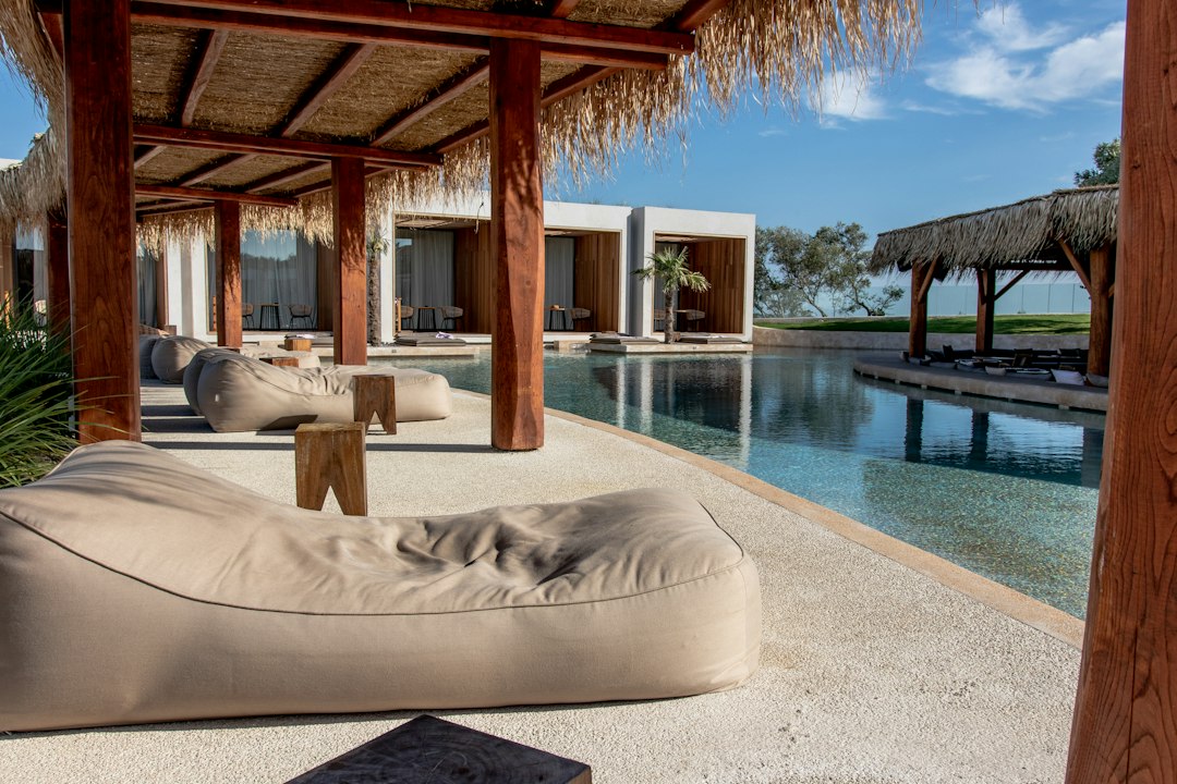 Modern poolside area with wooden pergolas, beige lounge chairs, and a view of a rectangular swimming pool bordered by contemporary Las Vegas buildings and luxury suites.