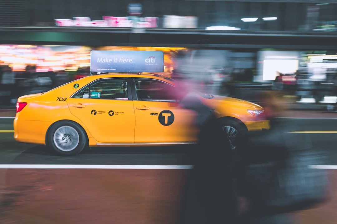 A yellow NYC taxi cab drives past blurred pedestrians on a New York City street at night, with a Citi advertisement on the roof, capturing the energy near high-end shopping districts.
