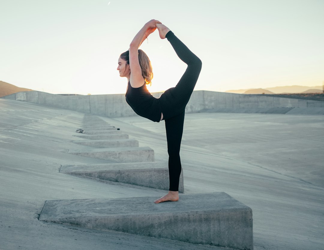 A person in black athletic wear performs a standing yoga pose on a concrete platform at sunset, embodying the tranquil atmosphere of high-end wellness and luxury fitness retreats in an inspiring outdoor setting.