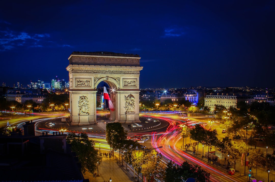 Nighttime view of the Arc de Triomphe in Paris, illuminated with traffic light trails circling the monument and city lights in the background—a must-see for anyone planning to travel to Paris or searching for the ultimate guide to this iconic city.
