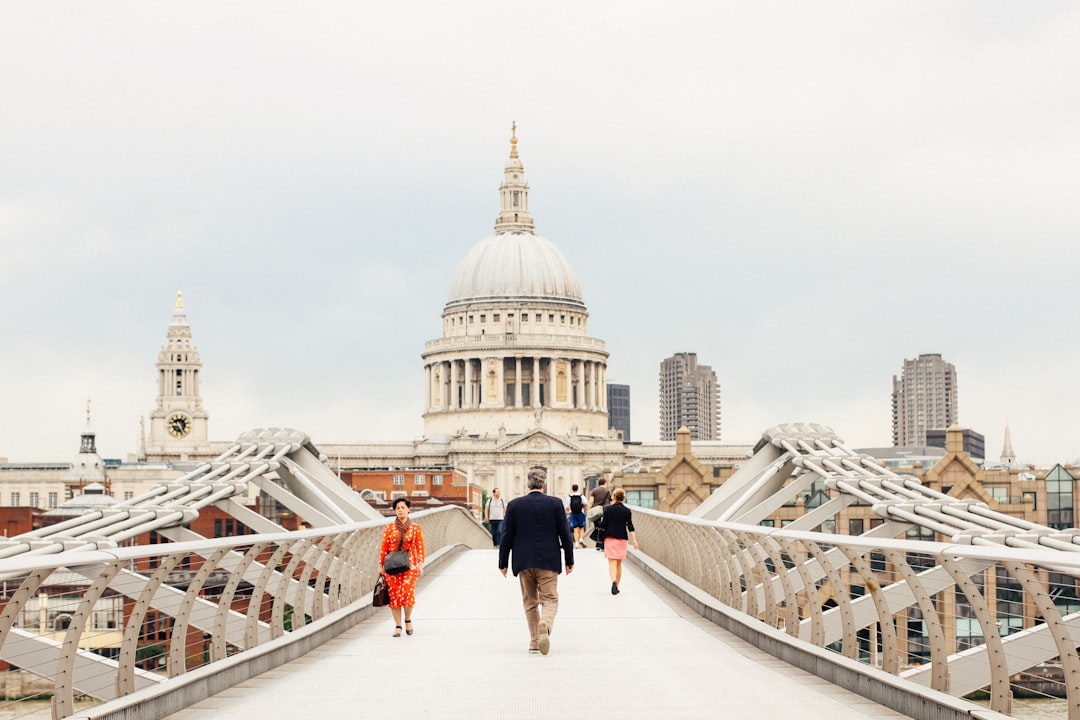 People walk across the Millennium Bridge in London, with St. Paul’s Cathedral and city buildings—including renowned Luxushotels London—visible in the background.