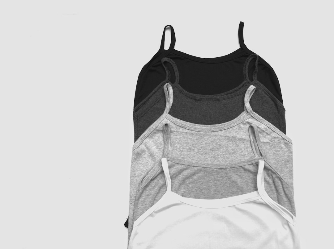 Four camisole tops in black, dark gray, light gray, and white are neatly stacked on a plain, light-colored background—perfect essentials for relaxation or luxurious stays at spa hotels worldwide.
