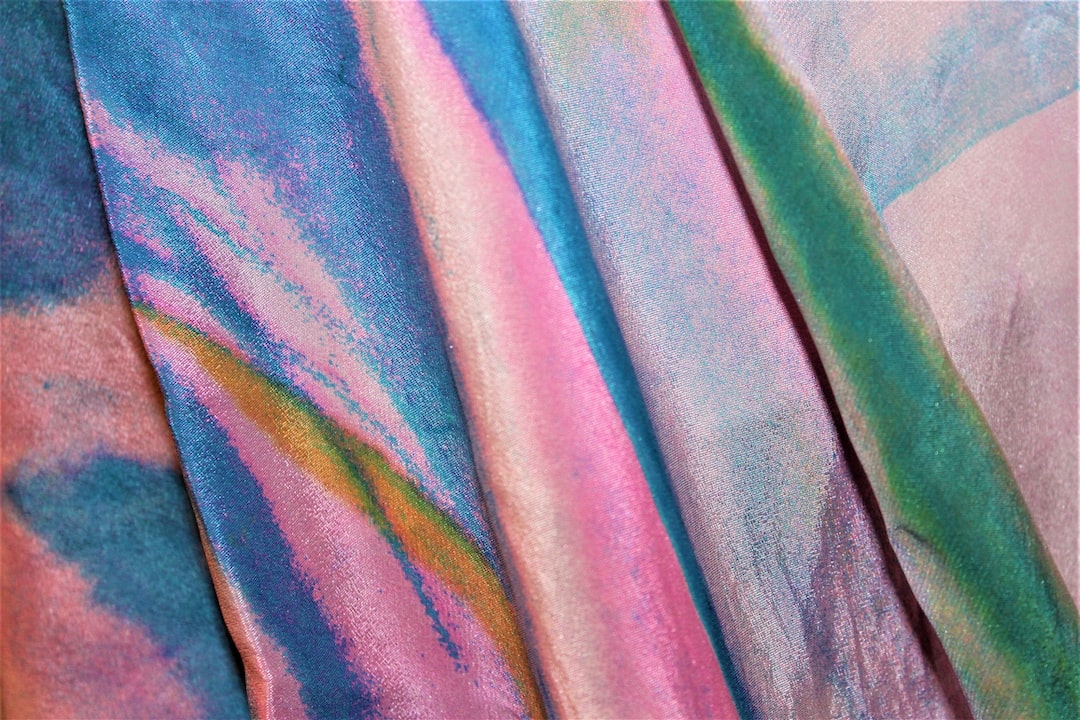 Close-up of colorful, iridescent fabric with flowing patterns in pink, blue, green, and purple shades—an innovative fabric reminiscent of Issey Miyake’s signature design.