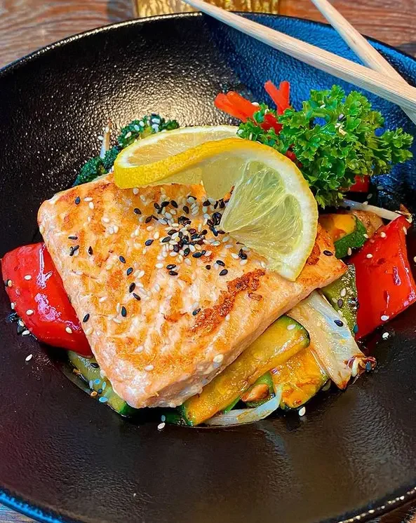 Pan seared salmon on wok vegetables in a black bowl