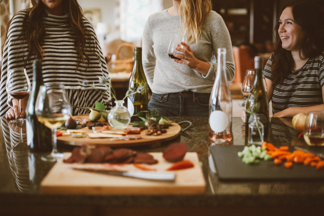 Three women stand around a kitchen island with wine glasses, talking and smiling, enjoying charcuterie and vegetables—capturing the relaxed elegance of luxury networking events.
