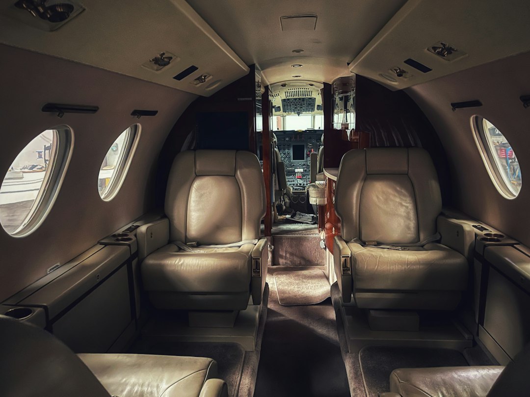 Experience luxury travel in the interior of a private jet, featuring four beige leather seats and a stunning view of the cockpit in the background.