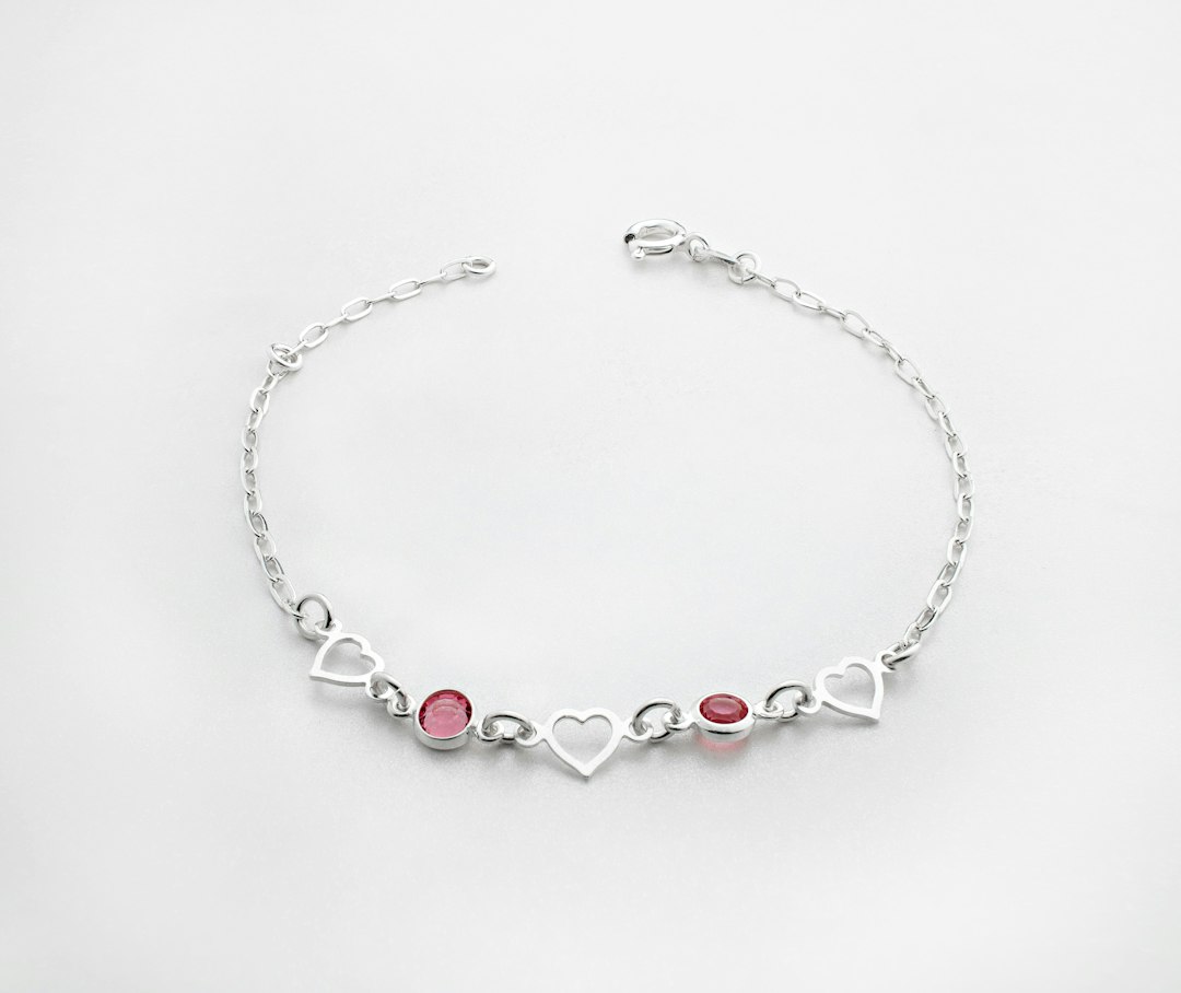 Silver chain bracelet with three open heart shapes and two pink gemstones arranged alternately in the center, perfect for those who love bold jewelry, displayed on a plain white background.