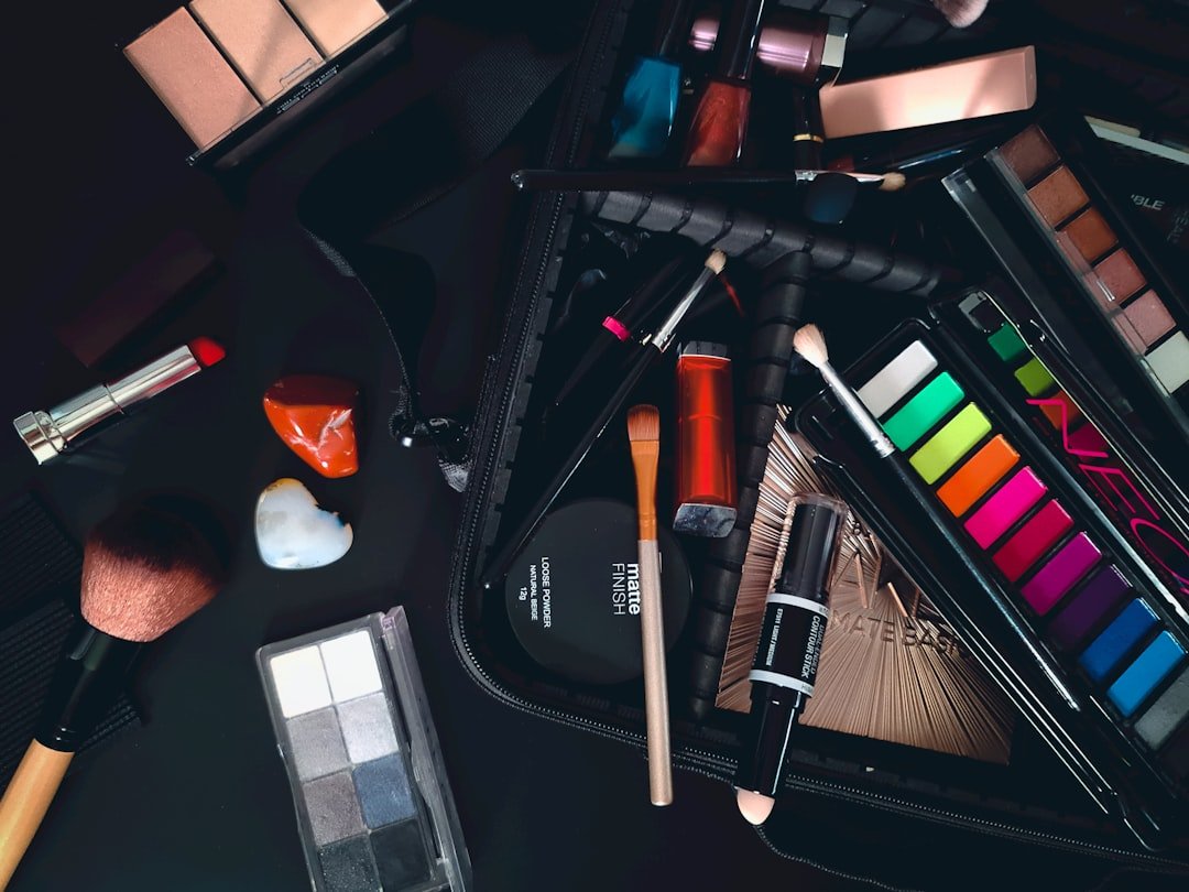 Assorted makeup products and tools, perfect for achieving an effortless beauty or natural look, including brushes, eyeshadow palettes, lipsticks, and blush, are spread out on a dark surface around a partially open makeup bag.