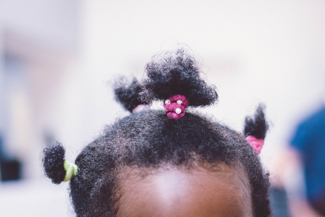 Close-up of a child's head showcasing healthy hair styled in several small puffs, each secured with colorful hair ties and beads—a playful look celebrating natural hair care.
