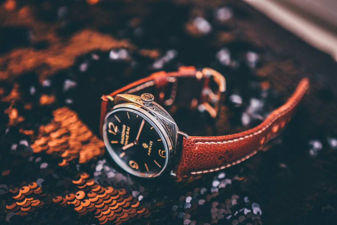 A wristwatch with a brown leather strap and black dial rests on a surface covered in black and orange sequins, capturing the elegance often seen at high-end watch auctions.