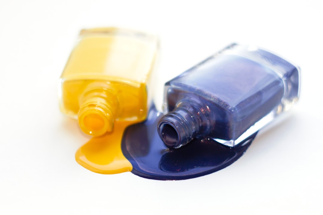 Two open nail polish bottles, one yellow and one dark blue, lie on their sides with spilled polish pooling on a white surface—a striking display of manicure fashion and new trends in nail art.